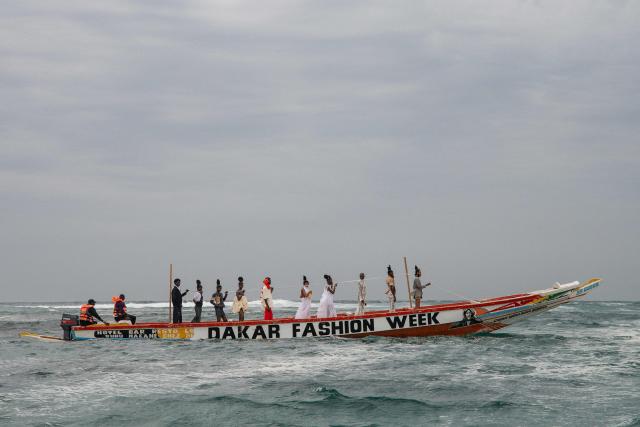 Models, wearing designs by the "Inspire" collection, ride on a pirogue during the final show of the Dakar Fashion Week in Ngor Bay, Dakar, Senegal, on December 6, 2025. (Photo by NICOLAS REMENE / AFP)