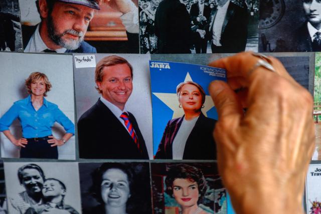 A woman selects a photo of Chilean presidential candidate Jeannette Jara of the Unidad por Chile coalition at a fair stall in Santiago, eight days before the presidential runoff, on December 6, 2025. Chile will choose its next president in a runoff on December 14, with far-right candidate Jose Antonio Kast as the clear favorite against leftist Jeannette Jara, after a campaign marked by fears over crime and irregular migrants. (Photo by Raul BRAVO / AFP)