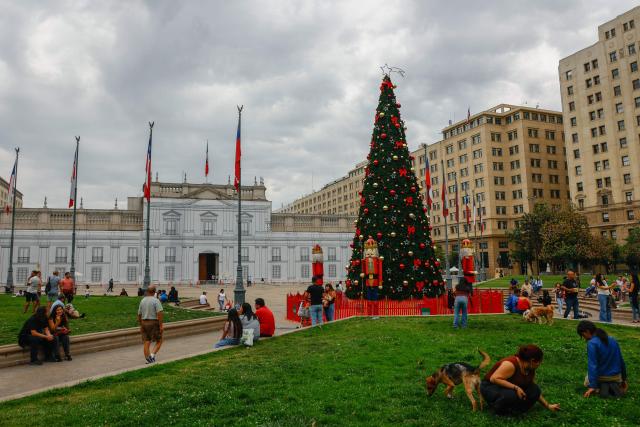 People walk past Christmas decorations in front of La Moneda presidential palace in Santiago, eight days before the presidential runoff election, on December 6, 2025. Chile will choose its next president in a runoff on December 14, with far-right candidate Jose Antonio Kast as the clear favorite against leftist Jeannette Jara, after a campaign marked by fears over crime and irregular migrants. (Photo by Raul BRAVO / AFP)