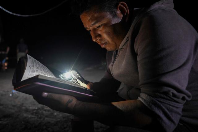 A relative of the victims reads a Bible during a vigil following a boat accident at the port of Iparia, in the Ucayali department of Peru’s central jungle, on December 6, 2025. At least 12 people, including three children, died on December 1, 2025, when a landslide sank two boats docked at a river port in central Peru, with dozens of others missing, officials said. (Photo by Hugo Alejos / AFP)