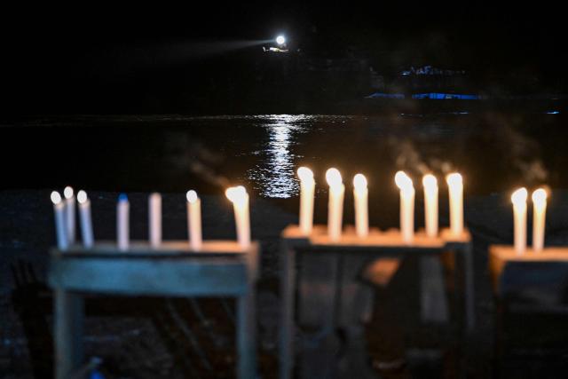 This view shows candles on the riverbank of the Ucayali during a vigil following a boat accident at the port of Iparia, in the Ucayali department of Peru’s central jungle, on December 6, 2025. At least 12 people, including three children, died on December 1, 2025, when a landslide sank two boats docked at a river port in central Peru, with dozens of others missing, officials said. (Photo by Hugo Alejos / AFP)