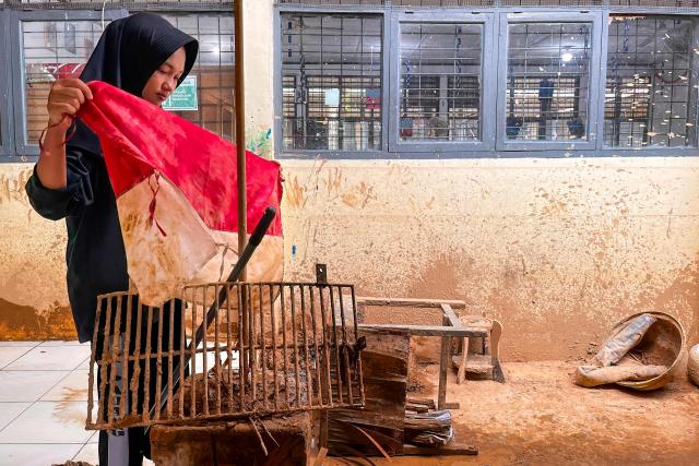A student folds a mud-stained Indonesian flag while cleaning her flood-affected school with other students and teachers in Padang, West Sumatra, on December 7, 2025. Ruinous floods and landslides have killed more than 900 people on Indonesia's island of Sumatra, the country's disaster management agency said on December 6, with fears that starvation could send the toll even higher. (Photo by Ade Yuandha / AFP)