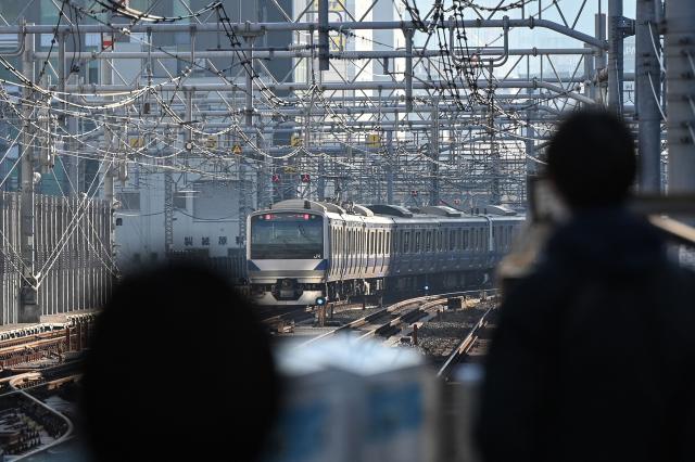 People watch a train pass through a station in Tokyo on December 7, 2025. (Photo by GREG BAKER / AFP)