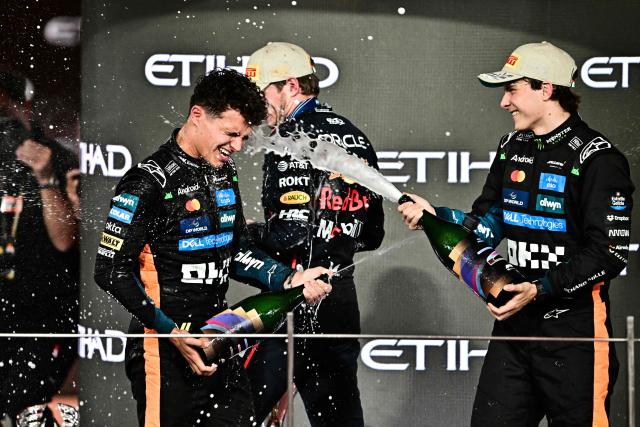 TOPSHOT - World champion and race third-placed McLaren's British driver Lando Norris (L) celebrates with race winner Red Bull Racing's Dutch driver Max Verstappen (C) and second-placed McLaren's Australian driver Oscar Piastri on the podium at the end of the Abu Dhabi Formula One Grand Prix at the Yas Marina Circuit in Abu Dhabi on December 7, 2025. (Photo by Giuseppe CACACE / AFP)