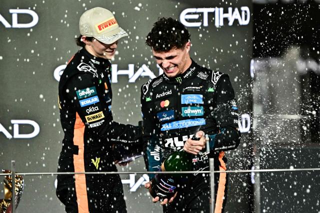 World champion and race third-placed McLaren's British driver Lando Norris (R) celebrates with teammate second-placed Australian driver Oscar Piastri on the podium at the end of the Abu Dhabi Formula One Grand Prix at the Yas Marina Circuit in Abu Dhabi on December 7, 2025. (Photo by Giuseppe CACACE / AFP)