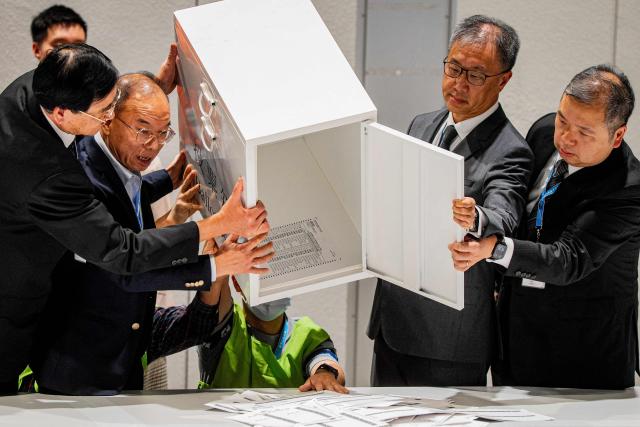 Secretary for Constitutional and Mainland Affairs Erick Tsang Kwok-wai (2L) helps empty the first ballot box after polls closed in the Legislative Council elections in Hong Kong, China, on December 7, 2025. (Photo by Leung Man Hei / AFP)
