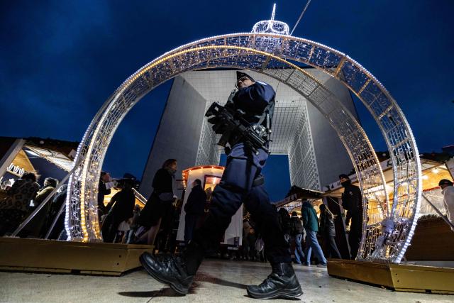 TOPSHOT - A French Republican Security Corps (CRS - Compagnies Republicaines de Securite) police officer patrols inside the Christmas market on the Parvis de La Defense, with the Grande Arche de la Defense in the background at the business district of La Defense, in Puteaux outside Paris, on December 7, 2025. (Photo by Ian LANGSDON / AFP)
