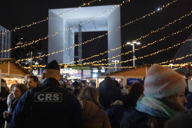 A French Republican Security Corps (CRS - Compagnies Republicaines de Securite) police officer patrols inside the Christmas market on the Parvis de La Defense, with the Grande Arche de la Defense in the background at the business district of La Defense, in Puteaux outside Paris, on December 7, 2025. (Photo by Ian LANGSDON / AFP)