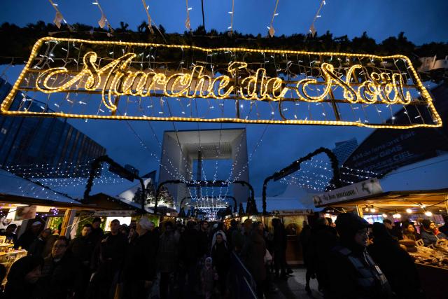 Visitors walk and shop at the Christmas market on the Parvis de La Defense, with La Grande Arche of La Defense in the background, at the business district of La Defense, in Puteaux outside Paris, on December 7, 2025. (Photo by Ian LANGSDON / AFP)