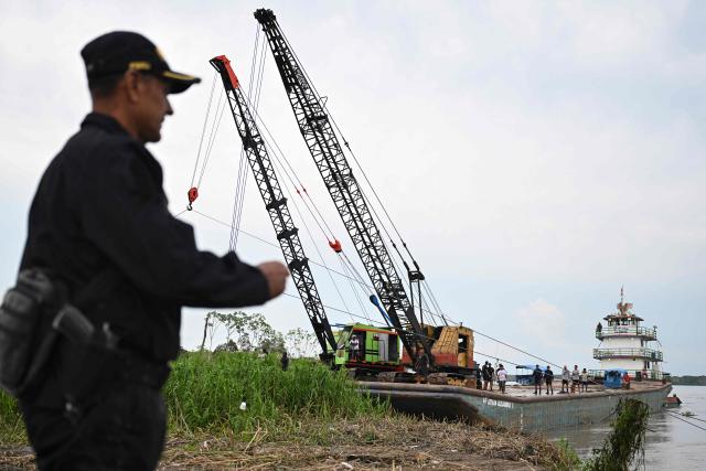 The crane that will be used to recover the wrecked boats arrives at the accident site at the port of Iparia in the Ucayali department in Peru's central jungle on December 7, 2025. At least 12 people, including three children, died on December 1, 2025, when a landslide buried two boats docked at a river port in central Peru, while dozens of others remain missing, officials said. (Photo by Hugo Alejos / AFP)