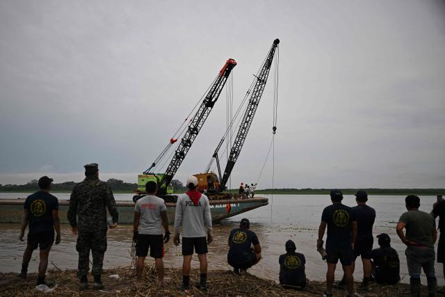 The crane that will be used to recover the wrecked boats arrives at the accident site at the port of Iparia in the Ucayali department in Peru's central jungle on December 7, 2025. At least 12 people, including three children, died on December 1, 2025, when a landslide buried two boats docked at a river port in central Peru, while dozens of others remain missing, officials said. (Photo by Hugo Alejos / AFP)