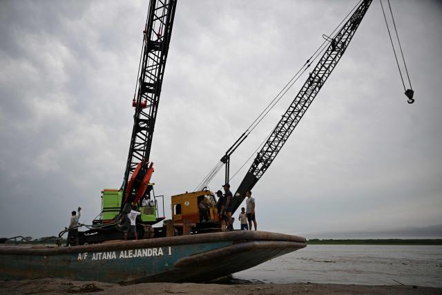 The crane that will be used to recover the wrecked boats arrives at the accident site at the port of Iparia in the Ucayali department in Peru's central jungle on December 7, 2025. At least 12 people, including three children, died on December 1, 2025, when a landslide buried two boats docked at a river port in central Peru, while dozens of others remain missing, officials said. (Photo by Hugo Alejos / AFP)