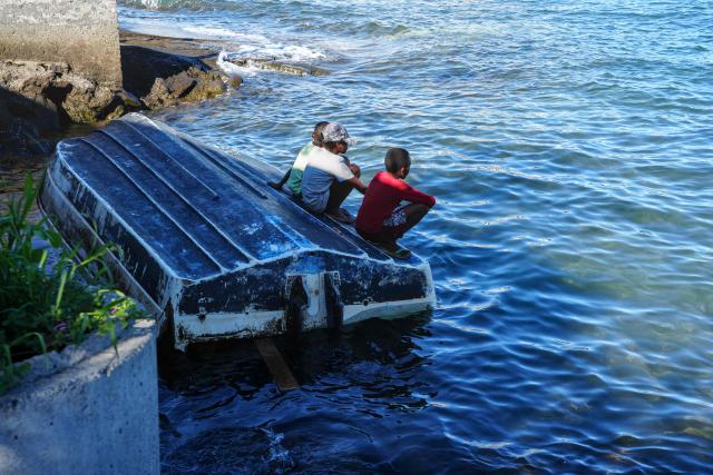 Children sit atop a boat wreck lying near the shore following the 2024 Cyclone Chido, in Mamoudzou, on the French Indian Ocean territory of Mayotte, on December 3, 2025. Chido, the most devastating cyclone to hit Mayotte in the last 90 years, hit France's poorest department on December 14, 2024, causing colossal damage. (Photo by Marine GACHET / AFP)