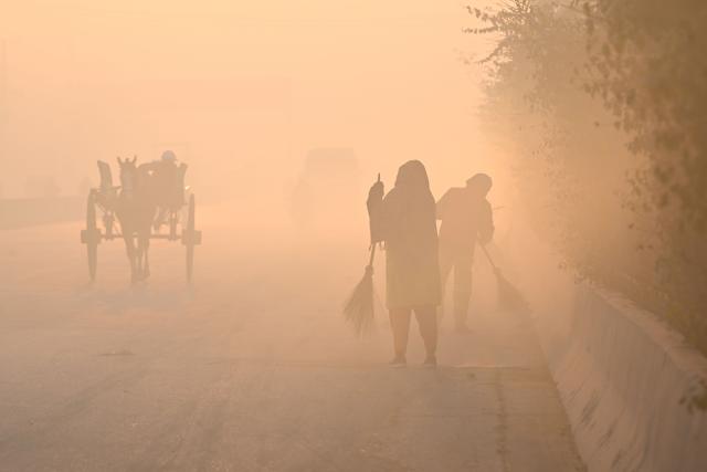 Workers sweep a road engulfed in smog in Lahore on December 8, 2025. (Photo by Arif ALI / AFP)