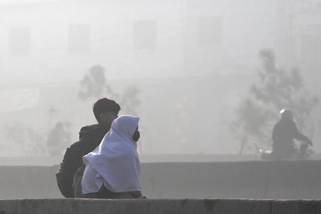 A school girl wearing a mask walks along a road amid dense smog in Lahore on December 8, 2025. (Photo by Arif ALI / AFP)