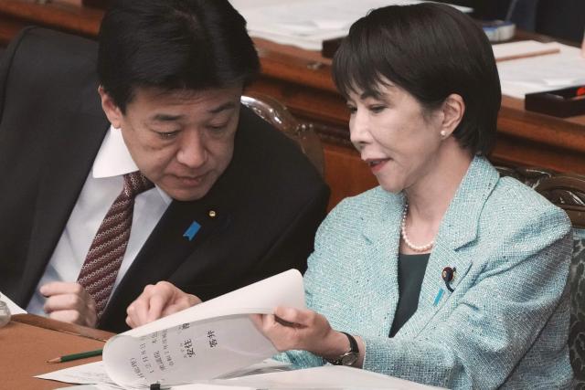 Japan's Prime Minister Sanae Takaichi (R) chats with Chief Cabinet Secretary Minoru Kihara during a plenary session of the House of Representatives at the National Diet in Tokyo on December 8, 2025. (Photo by Kazuhiro NOGI / AFP)