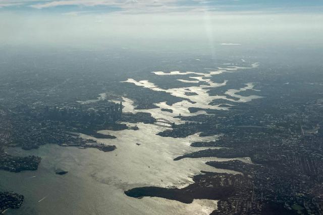 This photo shows an aerial view of smoke from bushfires burning on the outskirts of Sydney, hangs above Sydney Harbour on December 8, 2025. Dozens of bushfires burned along Australia's eastern seaboard on December 6, destroying several houses as a blistering heatwave set in. (Photo by DAVID GRAY / AFP)