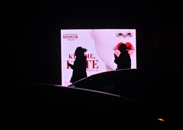 People walk past an advertising screen during blackout hours in Kyiv on December 7, 2025, amid the Russian invasion of Ukraine. (Photo by Sergei SUPINSKY / AFP)