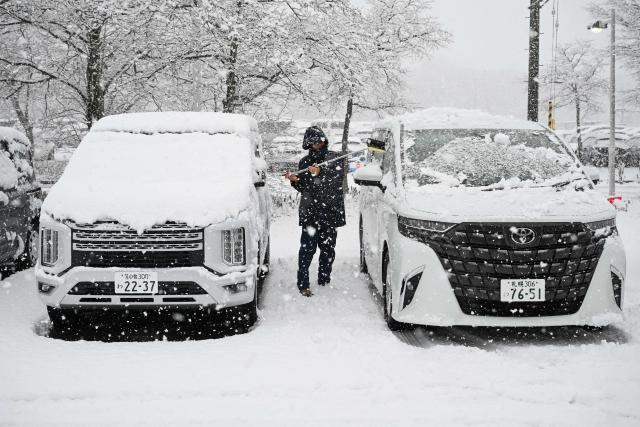 A man clears snow from cars in Chitose, in Japan’s northern Hokkaido prefecture on December 8, 2025. (Photo by GREG BAKER / AFP)