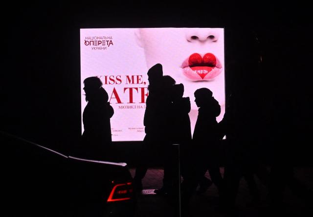 People walk past an advertising screen outside Kyiv Operetta Theater during blackout hours on December 7, 2025, amid the Russian invasion of Ukraine. (Photo by Sergei SUPINSKY / AFP)