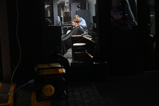 An power generator operates outside a barber shop while a hairdresser works with a client during blackout hours in Kyiv on December 7, 2025, amid the Russian invasion of Ukraine. (Photo by Sergei SUPINSKY / AFP)