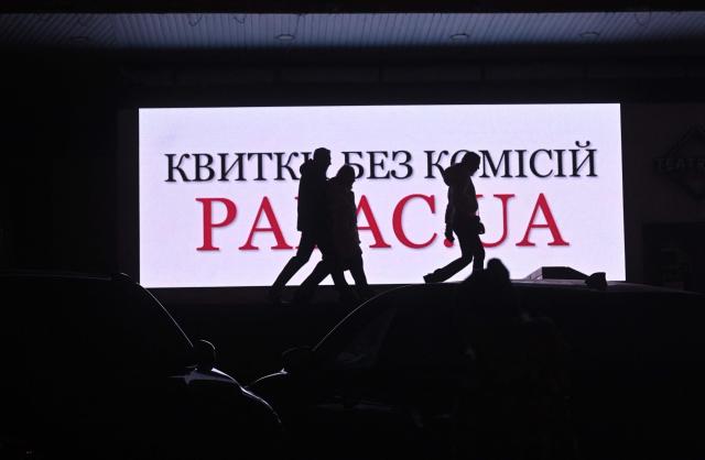 People walk past an advertising screen during blackout hours in Kyiv on December 7, 2025, amid the Russian invasion of Ukraine. (Photo by Sergei SUPINSKY / AFP)
