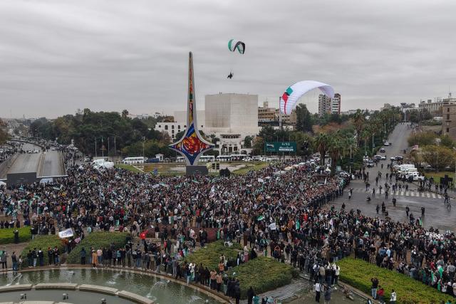 An areal photograph shows people watching a paraglider while celebrating a year since the ousting of longtime ruler Bashar al-Assad in the Syrian capital Damascus on December 8, 2025. President Ahmed al-Sharaa on December 8 urged Syrians to work together to rebuild their country as they marked a year since the ousting of longtime ruler Bashar al-Assad. Sharaa's Islamist-led alliance launched a lightning offensive in late November last year, taking the capital Damascus on December 8 after nearly 14 years of war and putting an end to more than five decades of the Assad family's iron-fisted rule. (Photo by Bakr ALKASEM / AFP)