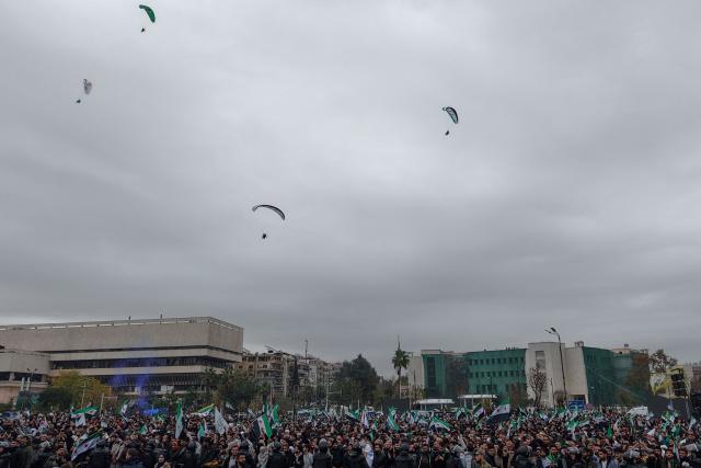 An areal photograph shows paragliders flying over people celebrating a year since the ousting of longtime ruler Bashar al-Assad in the Syrian capital Damascus on December 8, 2025. President Ahmed al-Sharaa on December 8 urged Syrians to work together to rebuild their country as they marked a year since the ousting of longtime ruler Bashar al-Assad. Sharaa's Islamist-led alliance launched a lightning offensive in late November last year, taking the capital Damascus on December 8 after nearly 14 years of war and putting an end to more than five decades of the Assad family's iron-fisted rule. (Photo by Bakr ALKASEM / AFP)
