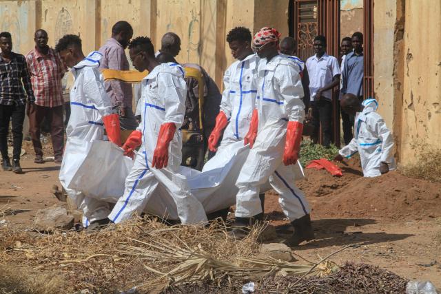 Members of the Red Crescent and others working for the authorities carry away a body bag as the exhumation and transfer of bodies from emergency burial sites inside schools, are taken to public cemeteries for burial, in the capital Khartoum on December 8, 2025. (Photo by Ebrahim Hamid / AFP)