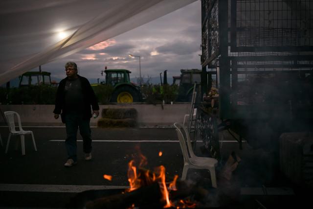 A farmer walks between parked tracktors blocking a national highway outside the central Greek city of Karditsa on December 8, 2025. Thousands of Greek farmers have since late November blocked highways, mainly in the centre and north of the country, to demand swifter access to EU subsidies delayed by an ongoing probe into multi-million fraud. (Photo by Aris MESSINIS / AFP)
