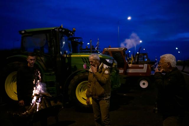 Farmers stand next to a fire in front of parked tracktors blocking a national highway outside the central Greek city of Karditsa on December 8, 2025. Thousands of Greek farmers have since late November blocked highways, mainly in the centre and north of the country, to demand swifter access to EU subsidies delayed by an ongoing probe into multi-million fraud. (Photo by Aris MESSINIS / AFP)