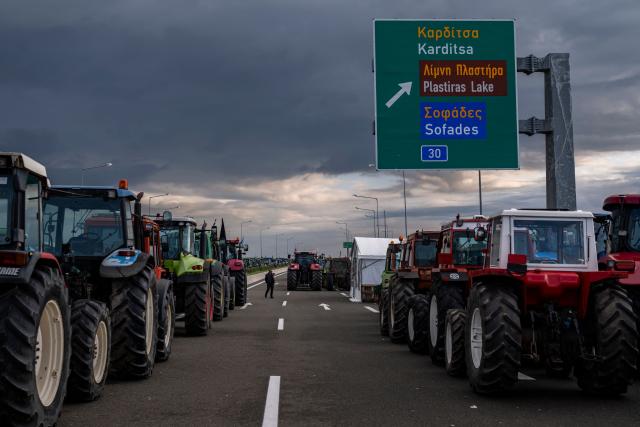 A farmer stands between parked tracktors blocking a national highway outside the central Greek city of Karditsa on December 8, 2025. Greek farmers demanding the payment of EU subsidies on December 8 shut down the two main international airports on the island of Crete after clashing with riot police in a growing showdown with the government. (Photo by Aris MESSINIS / AFP)