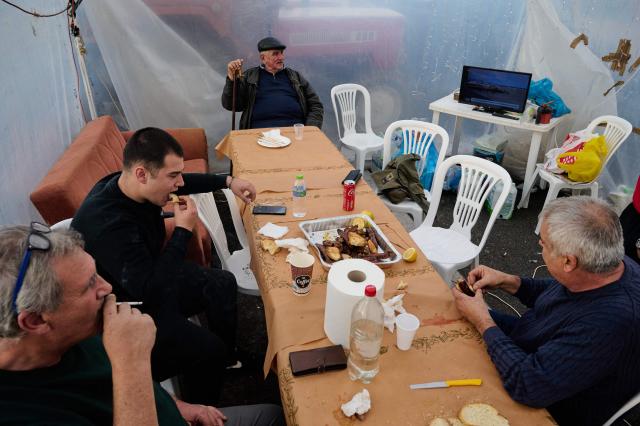 Farmers eat inside a makeshift tent as they block the national highway with their tractors outside the central Greek city of Karditsa on December 8, 2025 to demand swifter access to EU subsidies. Greek farmers demanding the payment of EU subsidies on December 8 shut down the two main international airports on the island of Crete after clashing with riot police in a growing showdown with the government. (Photo by Aggelos NAKKAS / AFP)
