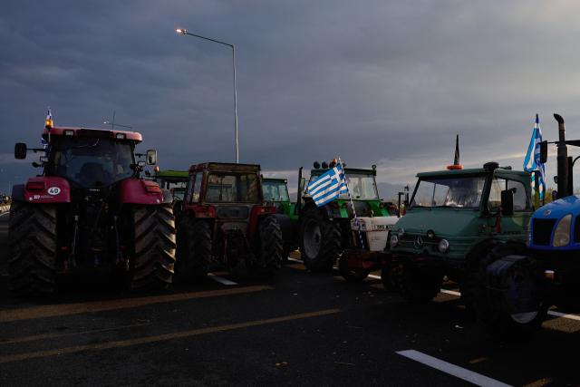 greece's national flags are installed on the tractors of farmers blocking the national highway outside the central Greek city of Karditsa on December 8, 2025 to demand swifter access to EU subsidies. Greek farmers demanding the payment of EU subsidies on December 8 shut down the two main international airports on the island of Crete after clashing with riot police in a growing showdown with the government. (Photo by Aggelos NAKKAS / AFP)