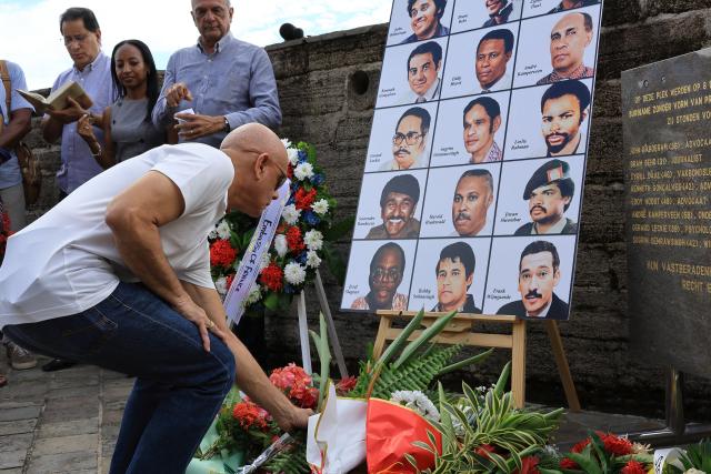 A relative of the 15 victims of the December 1982 murders at the former Fort Zeelandia military barracks lies flowers in front of their pictures during a remembrance ceremony in Paramaribo on December 8, 2025. Relatives of the 15 victims killed filed a lawsuit against the government demanding rehabilitation and compensation. (Photo by Ranu ABHELAKH / AFP)