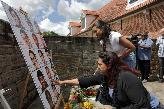 A relative of the 15 victims of the December 1982 murders at the former Fort Zeelandia military barracks touches their pictures during a remembrance ceremony in Paramaribo on December 8, 2025. Relatives of the 15 victims killed filed a lawsuit against the government demanding rehabilitation and compensation. (Photo by Ranu ABHELAKH / AFP)
