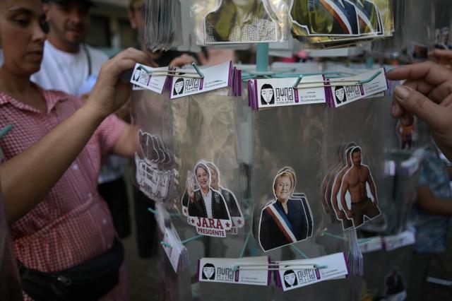 A woman sells stickers featuring images of Chilean presidential candidate Jeannette Jara of the Unidad por Chile coalition and former Chilean President Michelle Bachelet in Santiago on December 8, 2025. Chile will choose its next president in a runoff on December 14, 2025, with far-right candidate Jose Antonio Kast as the clear favorite against leftist Jeannette Jara, after a campaign marked by fears over crime and irregular migrants. (Photo by Eitan ABRAMOVICH / AFP)