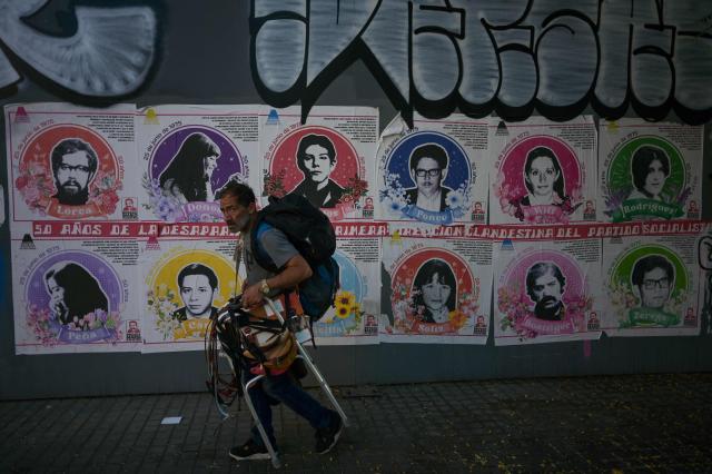 A belt vendor walks past images of Socialist Party leaders who were disappeared by former Chilean dictator Augusto Pinochet's secret police in 1975, at Larrastria neigborhood in Santiago on December 8, 2025. Chile will choose its next president in a runoff on December 14, 2025, with far-right candidate Jose Antonio Kast as the clear favorite against leftist Jeannette Jara, after a campaign marked by fears over crime and irregular migrants. (Photo by Eitan ABRAMOVICH / AFP)