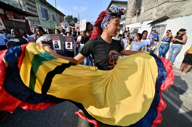 A relative of one of the four minors apprehended by soldiers and found dead near a military base, dances with a Ecuadorean flagged dress during a rally to demand justice a year after their apprehension in Guayaquil, Ecuador on December 8, 2025. (Photo by MARCOS PIN / AFP)