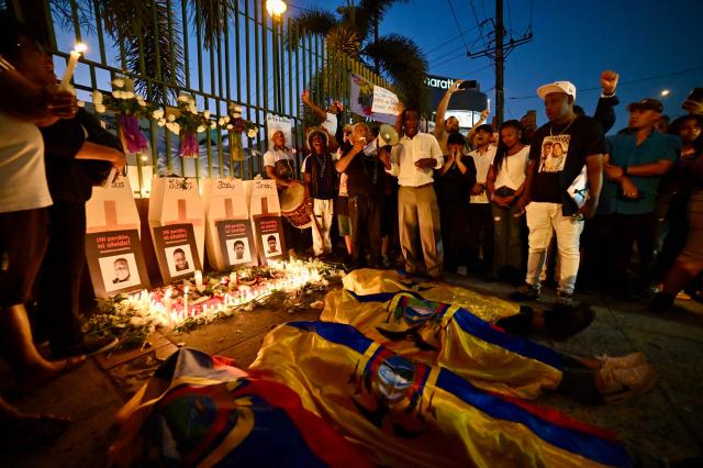 Relatives of the four minors apprehended by soldiers and found dead near a military base, lie on the ground covered with Ecuadorean flags during a rally to demand justice a year after their apprehension in Guayaquil, Ecuador on December 8, 2025. (Photo by MARCOS PIN / AFP)
