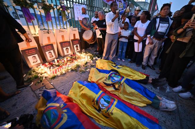 Relatives of the four minors apprehended by soldiers and found dead near a military base, lie on the ground covered with Ecuadorean flags during a rally to demand justice a year after their apprehension in Guayaquil, Ecuador on December 8, 2025. (Photo by MARCOS PIN / AFP)