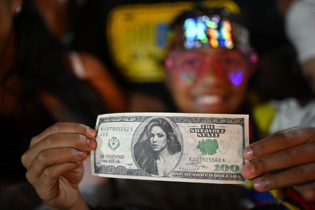 A fan of Colombian singer Shakira holds a fake dollar bill with her image  during her "Las mujeres ya no lloran" world tour at Velez Sarsfield stadium in Buenos Aires on December 8, 2025. (Photo by Luis ROBAYO / AFP)