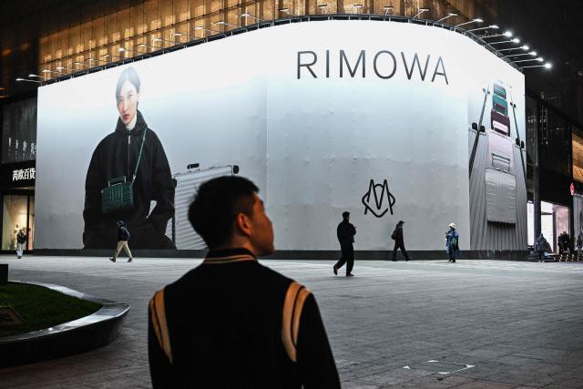 People walk past advertising in the Jing'an district of Shanghai on December 8, 2025. (Photo by Hector RETAMAL / AFP)