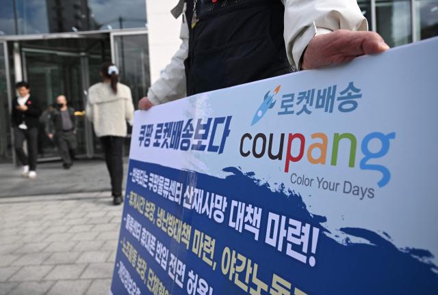 Transportation union members hold a placard showing the logo of South Korean online delivery service Coupang, during a protest to demand workers' rights outside a building housing the headquarters of Coupang in Seoul on December 9, 2025. South Korean police raided the Seoul headquarters of e-commerce giant Coupang on December 9, over a recent data leak believed to have affected almost two-thirds of the country's population. (Photo by Jung Yeon-je / AFP)