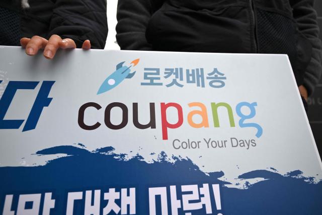 Transportation union members hold a placard showing the logo of South Korean online delivery service Coupang, during a protest to demand workers' rights outside a building housing the headquarters of Coupang in Seoul on December 9, 2025. South Korean police raided the Seoul headquarters of e-commerce giant Coupang on December 9, over a recent data leak believed to have affected almost two-thirds of the country's population. (Photo by Jung Yeon-je / AFP)