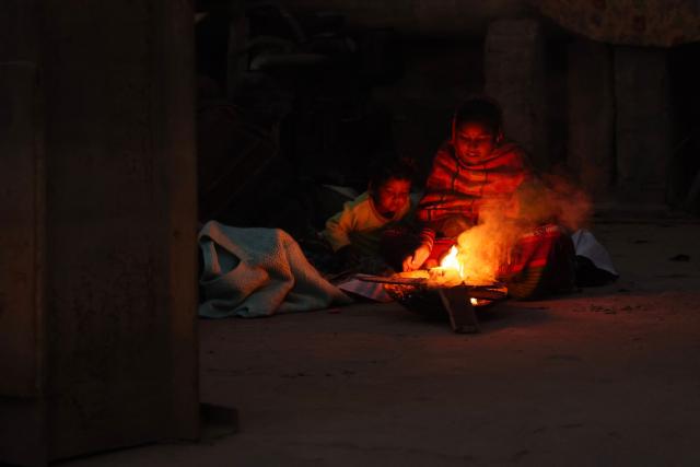 Homeless people keep themselves warm around a bonfire along a street in Varanasi on December 9, 2025. (Photo by Niharika KULKARNI / AFP)