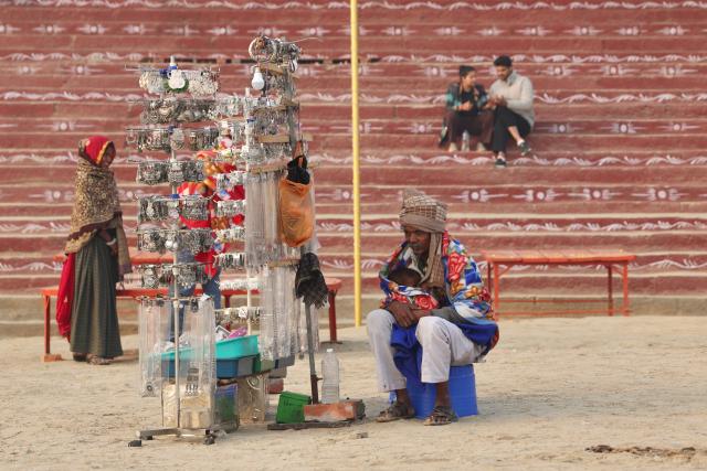 A jewellery vendor holds a child as he waits for customers at Assi Ghat along the banks of river Ganges in Varanasi on December 9, 2025. (Photo by Niharika KULKARNI / AFP)