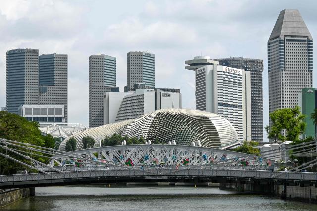 People walk across the Anderson bridge in the backdrop of the skyline in Singapore on December 9, 2025. (Photo by Roslan RAHMAN / AFP)