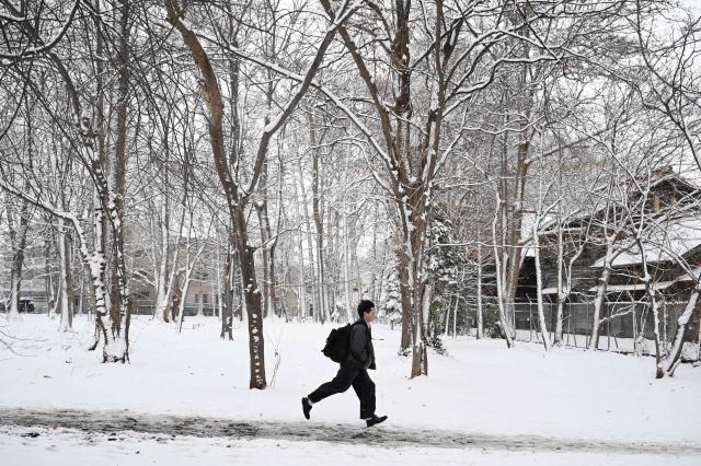 A man runs through the grounds of Hokkaido University after an overnight snowfall in Sapporo, in Japan’s northern Hokkaido prefecture on December 9, 2025. (Photo by GREG BAKER / AFP)