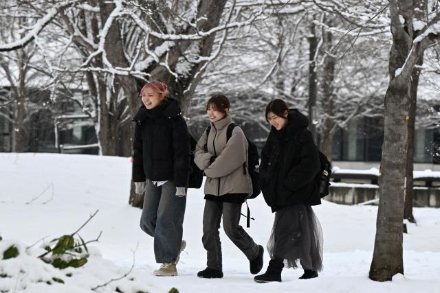 Women walk through the grounds of Hokkaido University after an overnight snowfall in Sapporo, in Japan’s northern Hokkaido prefecture on December 9, 2025. (Photo by GREG BAKER / AFP)